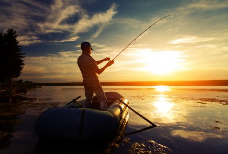 Fisherman with rod in the boat on the calm pond at sunset