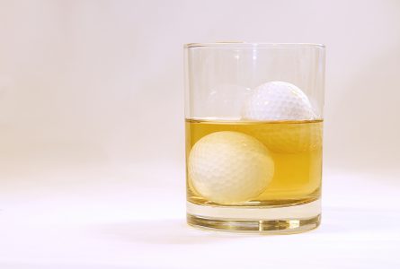 Image of a glass filled with alcohol with golf balls for ice cubes.